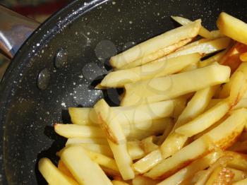 Fresh appetizing roasted potato chips in a frying pan close-up, in bright sunlight