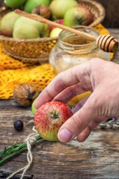 apple in hand on the background of the glass jar with fragrant honey and fruits