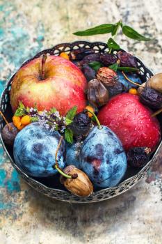 Ripe autumn apple and plum in an iron vase.