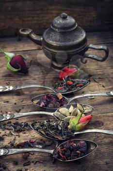 Stylish spoons with  variety of tea on vintage wooden board.