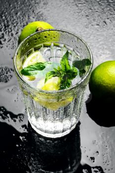 Glass cup with drink of water with lime on dark background