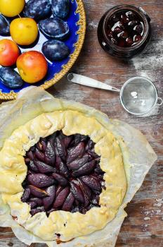 Rustic pie with plums and plum jam on wooden background