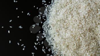 Pile of rice spill right on black background. Agriculture food raw seed. Closeup macro photo