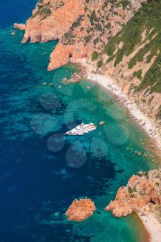 Luxury white pleasure yacht anchored near rocky beach of Corsica island, vertical photo, birds eye view 