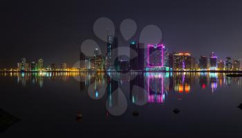 Night modern city skyline panorama with shining neon lights and reflection in the water. Manama, the Capital of Bahrain, Middle East