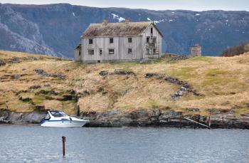 Old abandoned gray wooden house and small modern motorboat on the seacoast in Norway