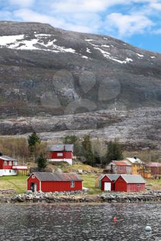 Traditional small Norwegian village with red wooden houses on rocky coast with mountains on the horizon