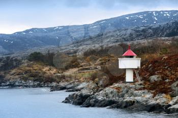 Norwegian lighthouse. White tower with red top stands on coastal rocks