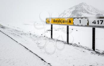 Yellow Icelandic road sign with direction to Reykjavik city stands on the roadside in cold snowy winter day