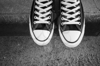 Black and white new sneakers, teenager feet stand on urban road border. top view. Closeup photo with selective focus