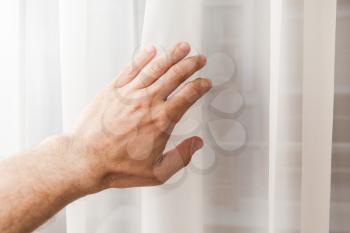 Male hand opens soft white tulle on window, first person view