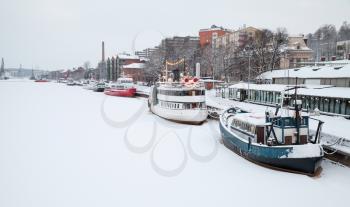Small boats are moored near river coast. Winter landscape of Turku town, Finland