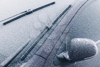 Car wipers on windshield and mirror covered with frost in cold winter season