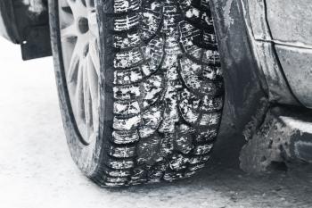 Close-up photo of car wheel on snow tire with metal studs, which improve traction on icy surfaces.