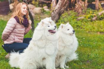 Smiling Caucasian girl with white Samoyed dogs walk in park, outdoor portrait