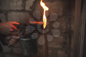Old rusty blowtorch with fire in male hands