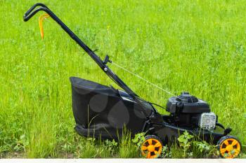 Modern gasoline powered lawn mower stands on fresh green grass, closeup photo, side view