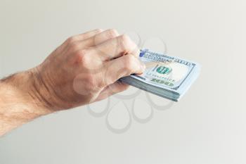 Bundle of One Hundred Dollars notes in hand over white wall background