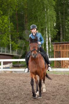 Riding lessons, teenage Caucasian girl rides a horse on riding field, vertical photo