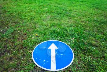 Ahead only, round blue road sign with white arrow lays on fresh green grass