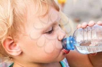Blond Caucasian child drink water from plastic bottle, close up outdoor photo