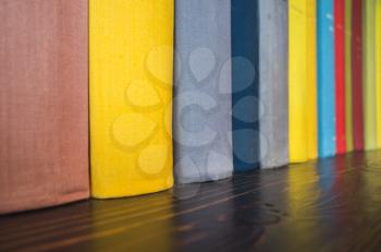 Colorful books stand in a row on wooden shelf