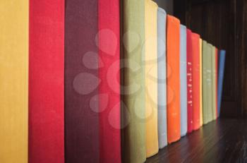 Old books in bright colorful covers stand in a row on wooden shelf