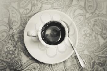 Freshly brewed espresso coffee in white cup stands on table. Closeup monochrome photo with selective focus