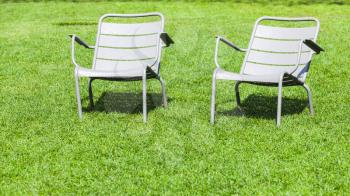 Two outdoor metal chairs stand on fresh green grass in summer park