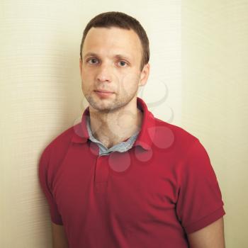 Studio portrait of young adult European man in red polo shirt, square frame
