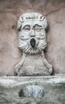 Ancient fountain with drinking water in the shape of a male face. Fermo, Italy