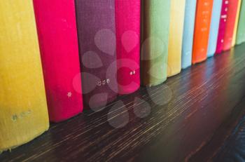 Books in colorful covers stand in a row on dark wooden shelf