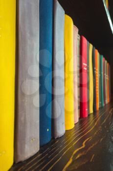 Books in colorful covers stand on wooden shelf, vertical photo