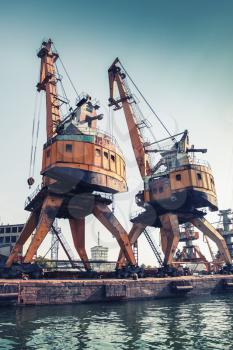 Huge port cranes stand on the pier in Burgas harbor, Black Sea, Bulgaria. vintage toned photo with tonal correction filter effect