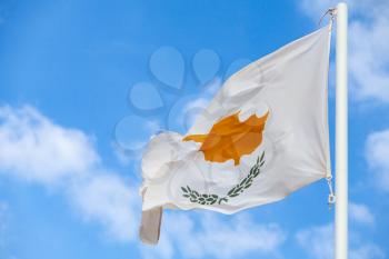 National flag of Cyprus on a flagpole over cloudy blue sky