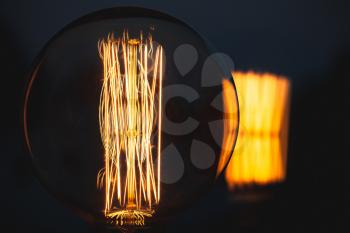 Retro stylized large tungsten lamp glowing over dark background, close-up photo with selective focus and shallow DOF