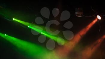 Red and green scenic spot lights with strong beams in smoke over dark background, modern stage illumination equipment