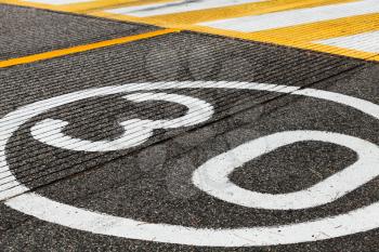 Speed limit road marking before pedestrian crossing on dark gray asphalt