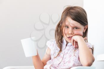 Portrait of little girl with cup of hot chocolate, close-up photo over white wall background