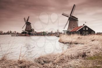 Wooden windmills on Zaan river coast, Zaanse Schans town, popular tourist attractions of the Netherlands. Suburb of Amsterdam. Photo with warm gradient tonal correction filter effect
