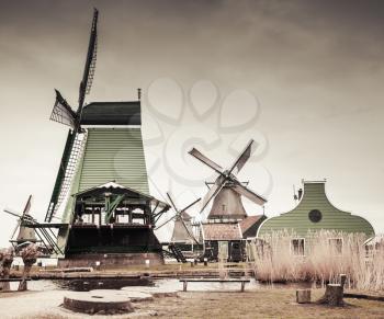 Wooden barns and windmills on Zaan river coast, Zaanse Schans town, popular tourist attractions of the Netherlands. Suburb of Amsterdam. Retro stylized photo with gradient tonal correction filter