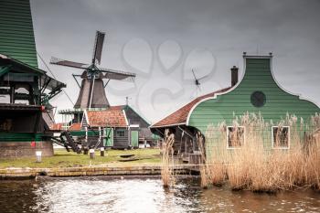 Old wooden barns and windmill on Zaan river coast. Zaanse Schans, popular tourist attractions of the Netherlands. Suburb of Amsterdam