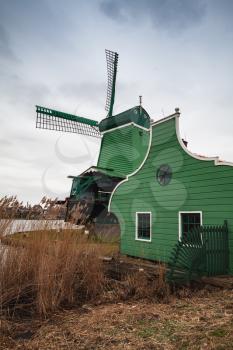 Windmill and green barn on Zaan river coast, Zaanse Schans town, popular tourist attractions of the Netherlands. Suburb of Amsterdam