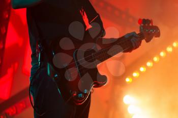 Electric bass guitar player in bright stage lights, close-up silhouette photo with soft selective focus