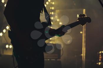 Electric bass guitar player on the stage, live hard rock music theme, vintage stylized photo with tonal correction filter effect