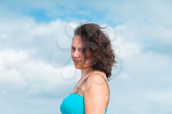 Smiling young adult Caucasian woman in blue dress, outdoor portrait over cloudy sky