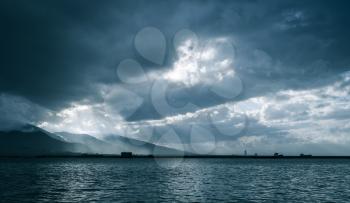 Dark clouds and sunlight, landscape background photo. Bay of Izmir, Turkey. Blue toned photo