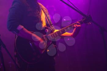 Guitarist plays on electric guitar in purple scenic illumination, soft selective focus