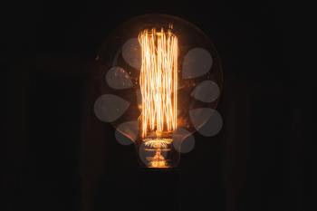 Vintage stylized tungsten lamp glowing in dark, close-up photo with selective focus and shallow DOF
