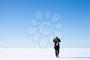 Teenage girl walks along the endless snowfield under bright blue winter sky